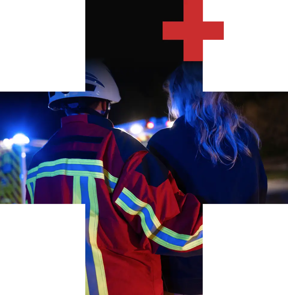 Sanitäter in Einsatzkleidung begleitet eine Frau bei einem nächtlichen Einsatz mit Blaulicht im Hintergrund.