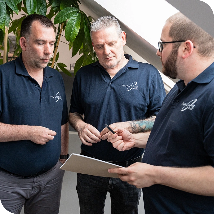 Drei ParaQare Mitarbeiter stehen zusammen und besprechen Unterlagen während einer Teamsitzung.